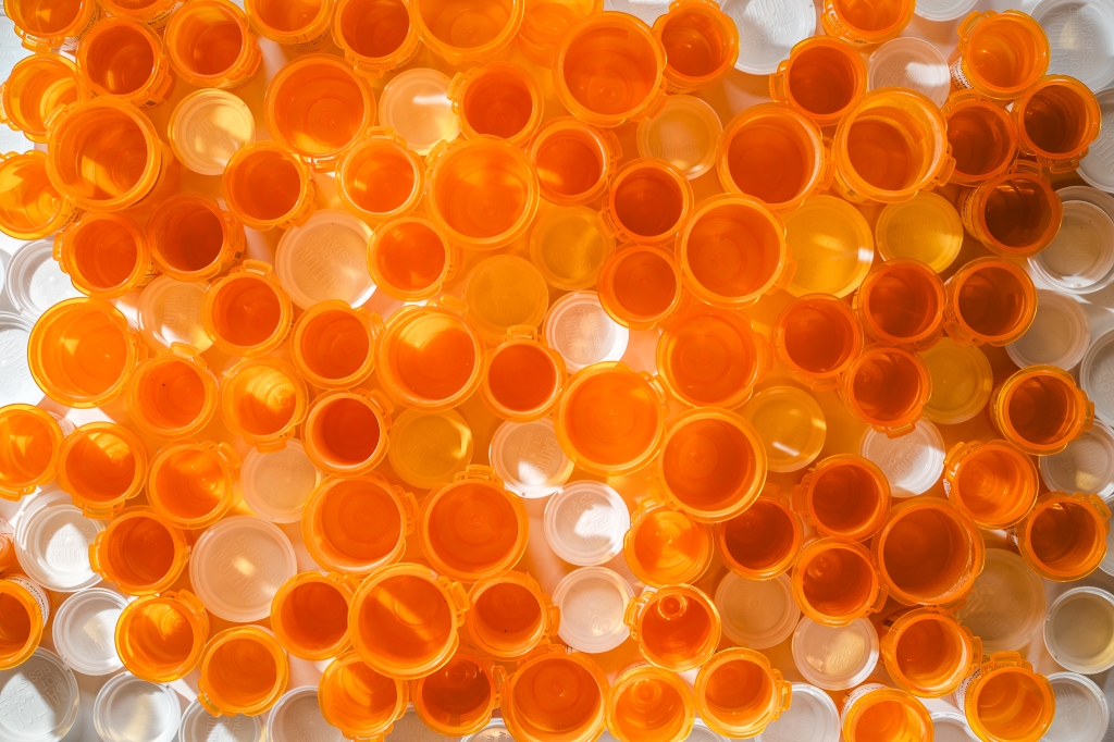 Dozens of empty orange pill bottles and lids arranged together, photographed from above.